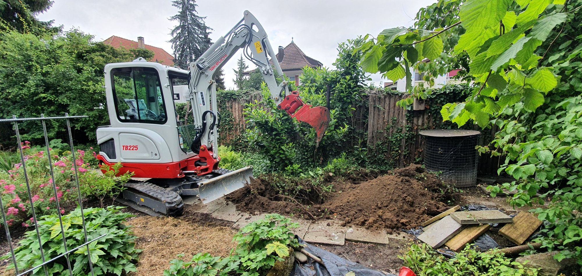 Minibagger arbeitet in einem bepflanzten Garten