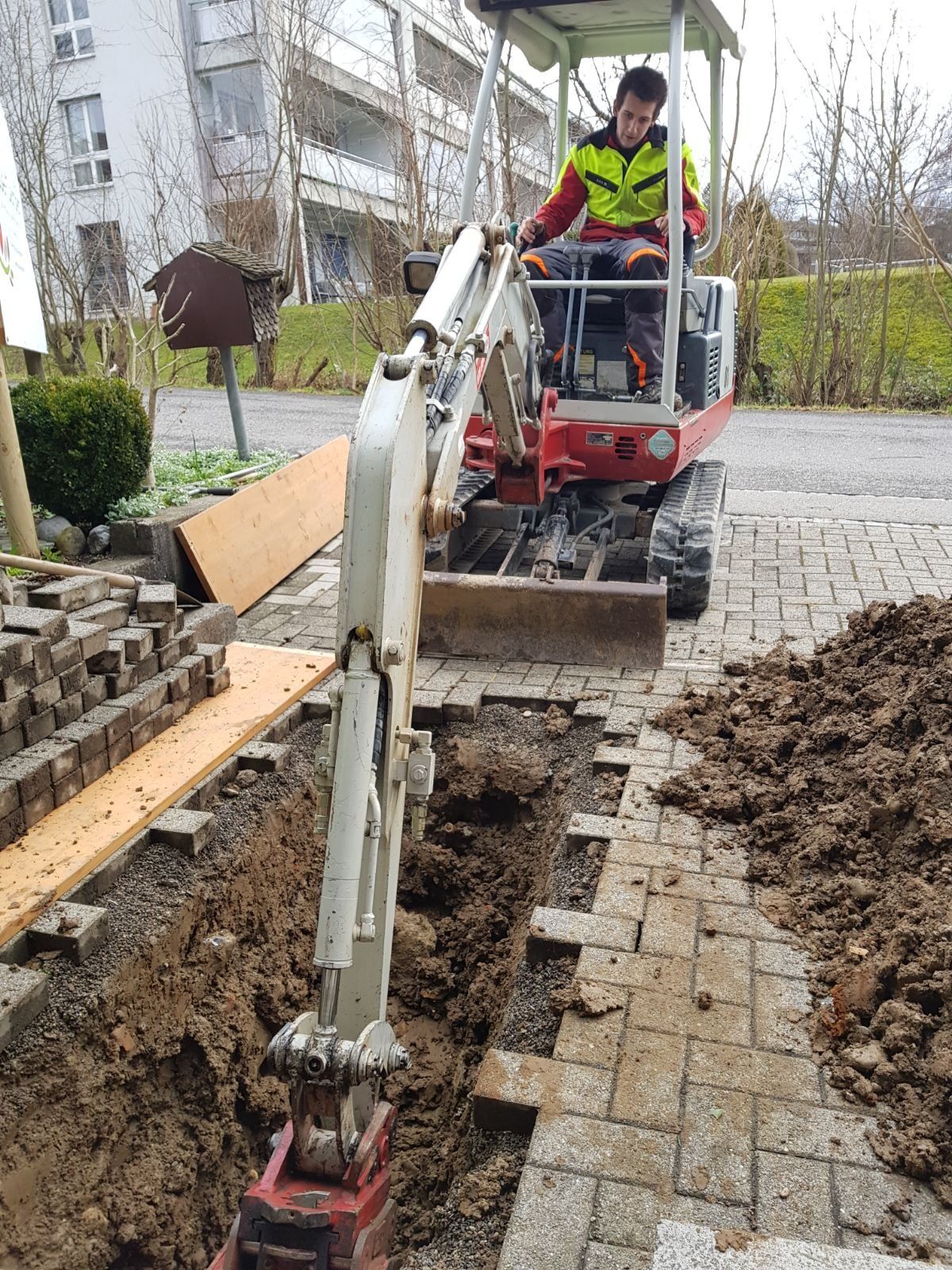 Bagger legt einen Graben im gepflästerten Weg frei